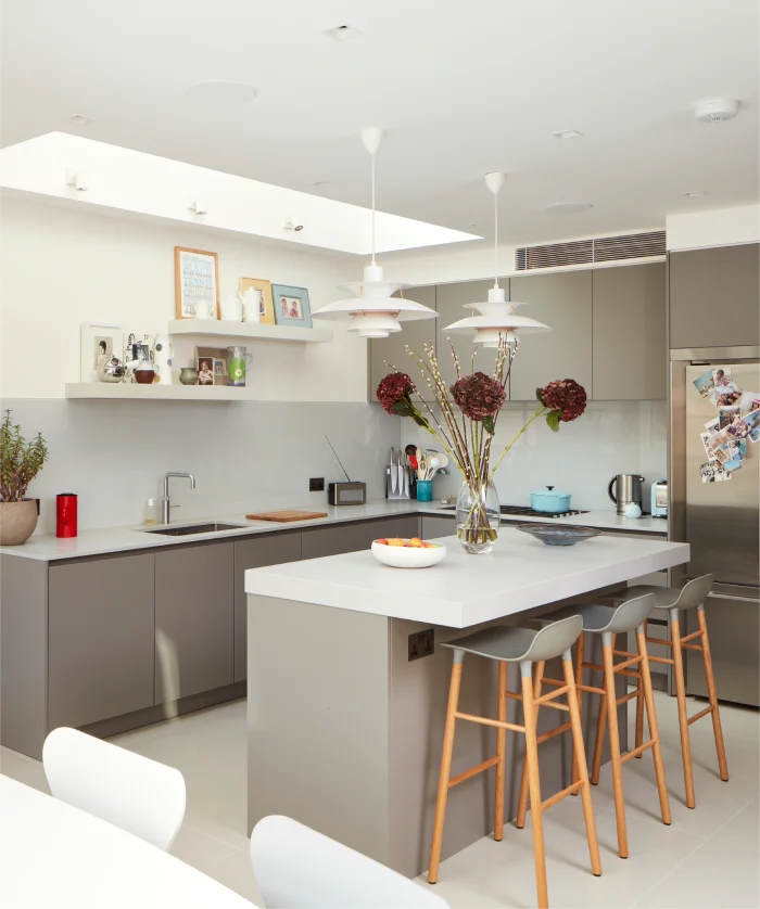 Modern kitchen with gray cabinets, white countertops, bar stools, pendant lights, and vibrant decor.