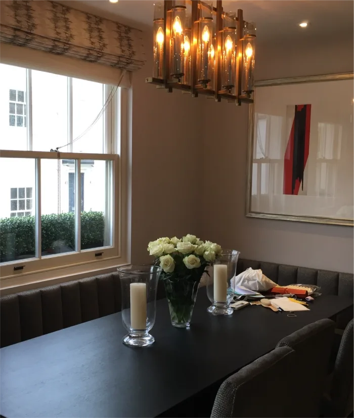 A cozy dining area with a contemporary touch, featuring a black table, upholstered seating, a centerpiece of fresh white roses, and a striking chandelier casting warm light over the setting.