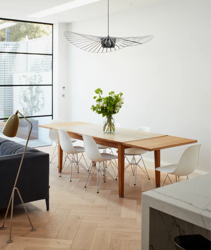 Bright dining space featuring a wooden table, modern white chairs, and a striking black pendant light fixture.