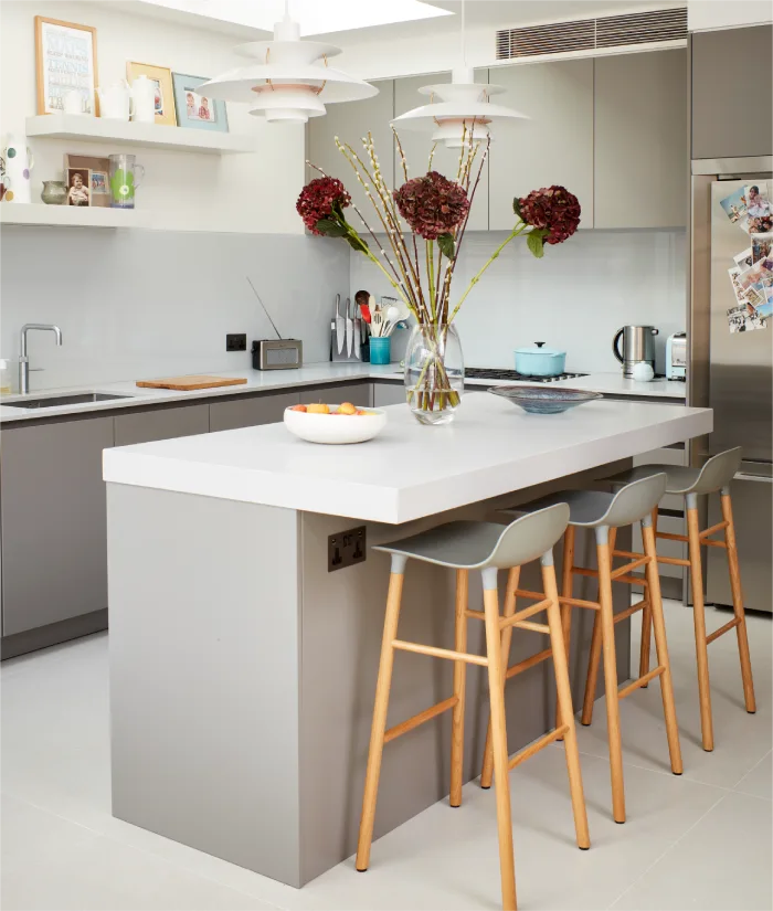 A modern kitchen featuring sleek gray cabinetry, a white quartz island with wooden barstools, pendant lights above, and elegant floral decor creating a welcoming ambiance.