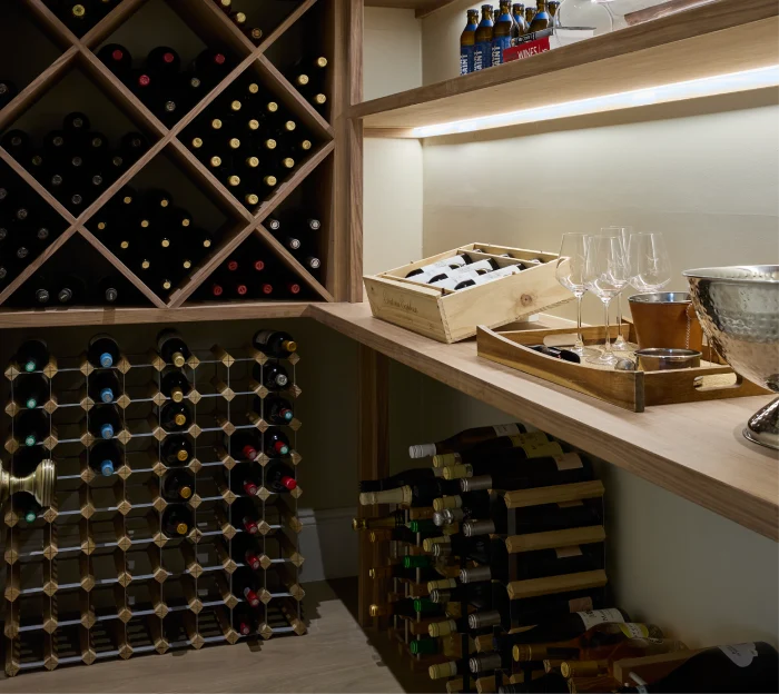 Luxury wine cellar with wooden racks, illuminated shelving, wine bottles, glasses, and a silver ice bucket.