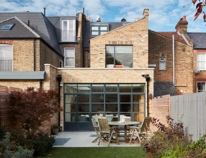 Brick home with modern loft conversion, large glass doors, outdoor dining area, and a landscaped garden.