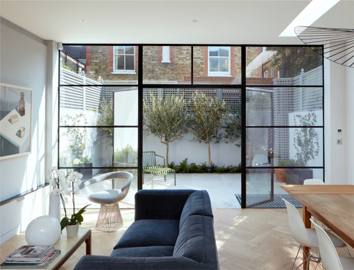 Bright living room with large glass doors, blue sofa, modern decor, and a view of a landscaped courtyard.