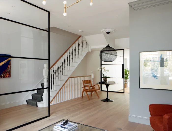 Elegant home interior with a white staircase, glass partitions, a black pendant light, and a wooden chair in a spacious, modern layout.