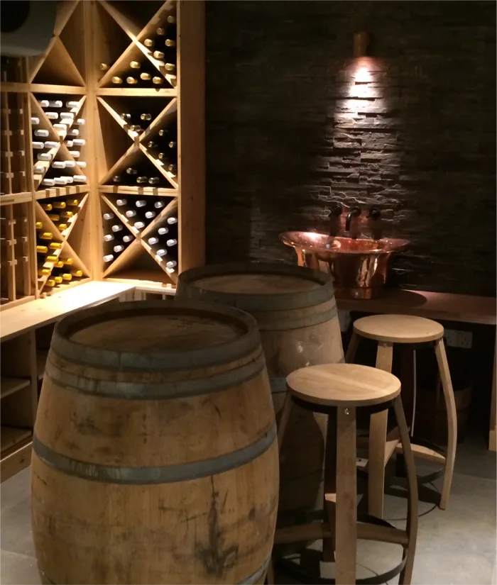 Rustic wine cellar featuring wooden barrels, geometric wine racks, and a stylish copper sink accent.