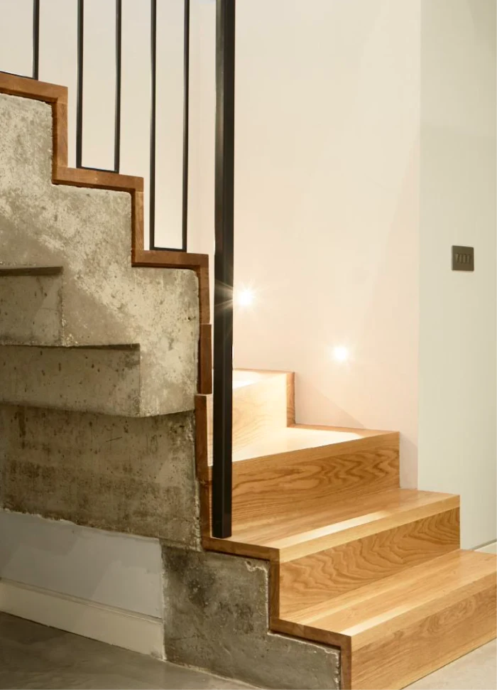 Modern staircase with a combination of raw concrete and polished wooden steps, accented by sleek black railings and built-in step lighting.