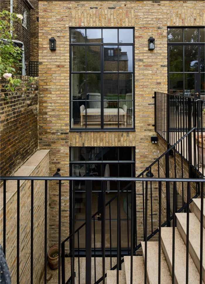 Modern brick facade with large black-framed windows, outdoor stairs, and a balcony railing.