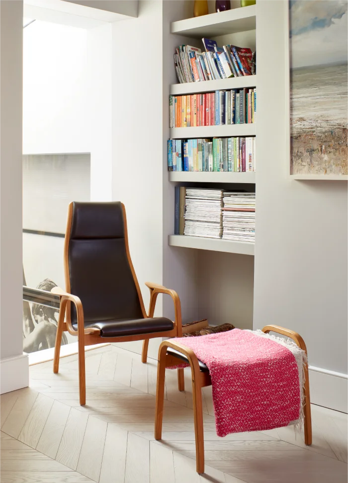 Cozy reading nook with a modern leather chair, matching footrest, and built-in shelves filled with books.