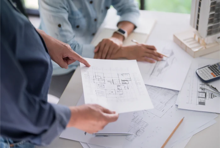 Architects discussing building plans with blueprints, scale models, and tools on the table during a project meeting