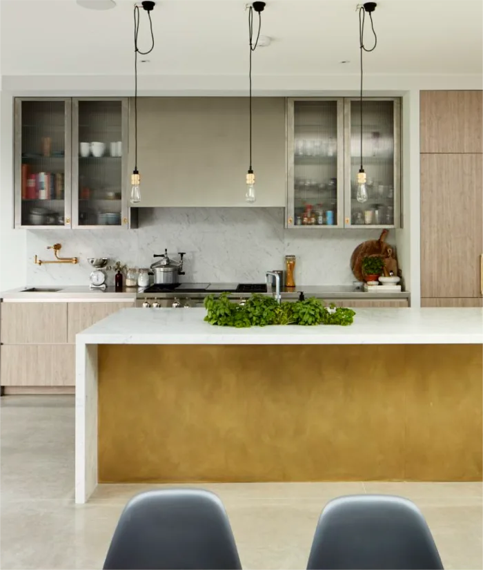 Modern kitchen with a marble island, gold-accented base, glass-front cabinets, and hanging pendant lights.