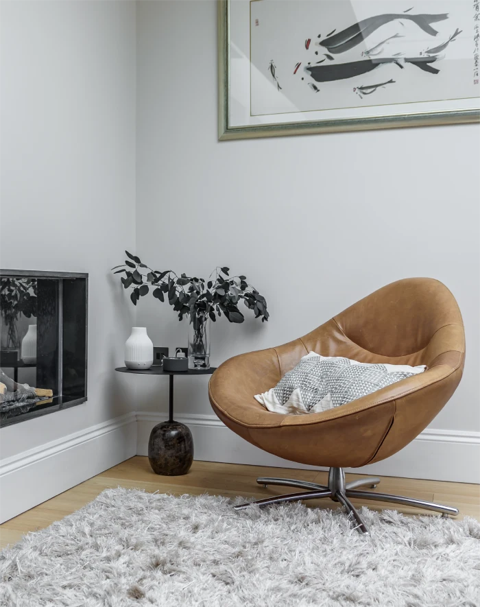 Modern living space with a leather swivel chair, textured rug, minimalist decor, and a framed abstract artwork.