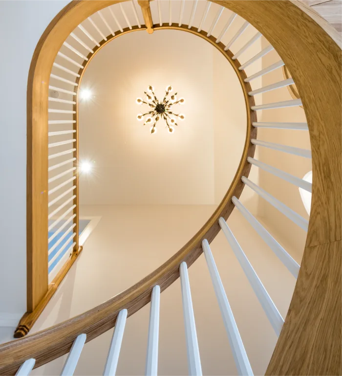 Elegant curved wooden staircase with white balustrades, featuring a modern chandelier and soft lighting above.