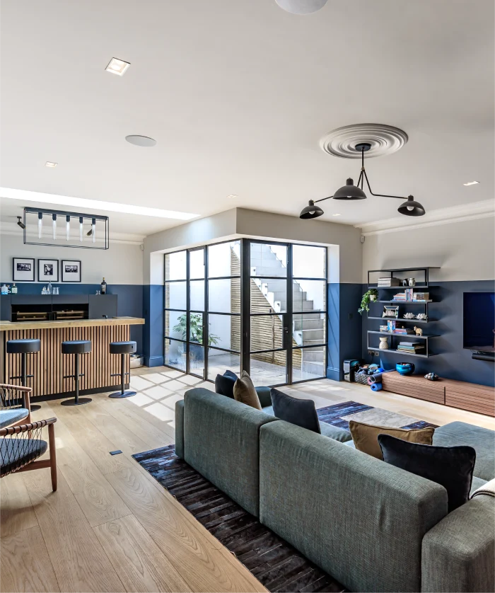 Modern open-plan living space with a cozy gray sofa, stylish bar area, glass doors, and sleek shelving.