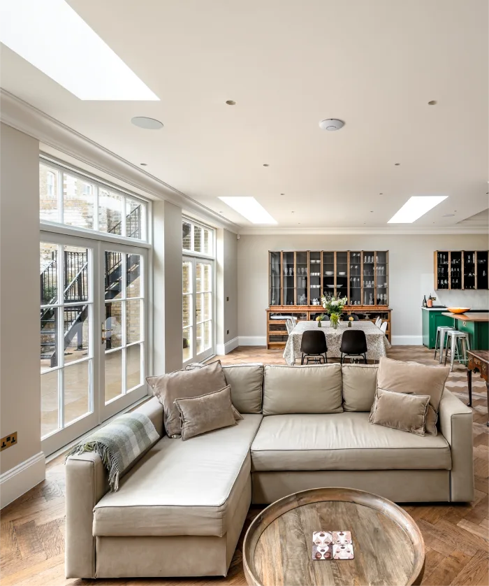 Bright and spacious open-plan living area featuring a cozy beige sectional, round wooden table, and dining space.