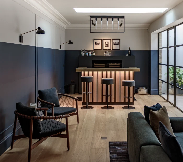 Modern home bar with a minimalist vibe, warm wood tones, cozy seating, and ample natural light from glass doors.