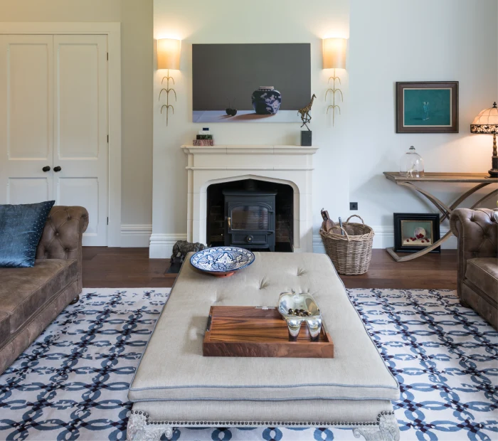 Cozy living room with a fireplace, tufted ottoman, decorative tray, and soft lighting accents.