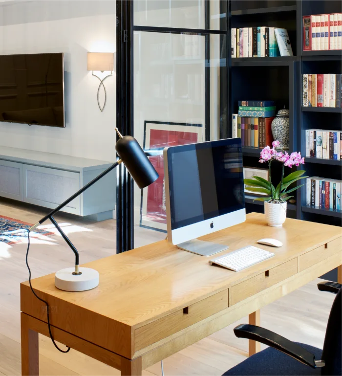 Modern home office with a sleek desk, iMac, black desk lamp, and built-in bookshelves in a bright, open space.