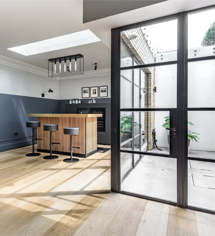 Bright and modern home bar with wooden accents, glass doors, and natural light from a skylight.