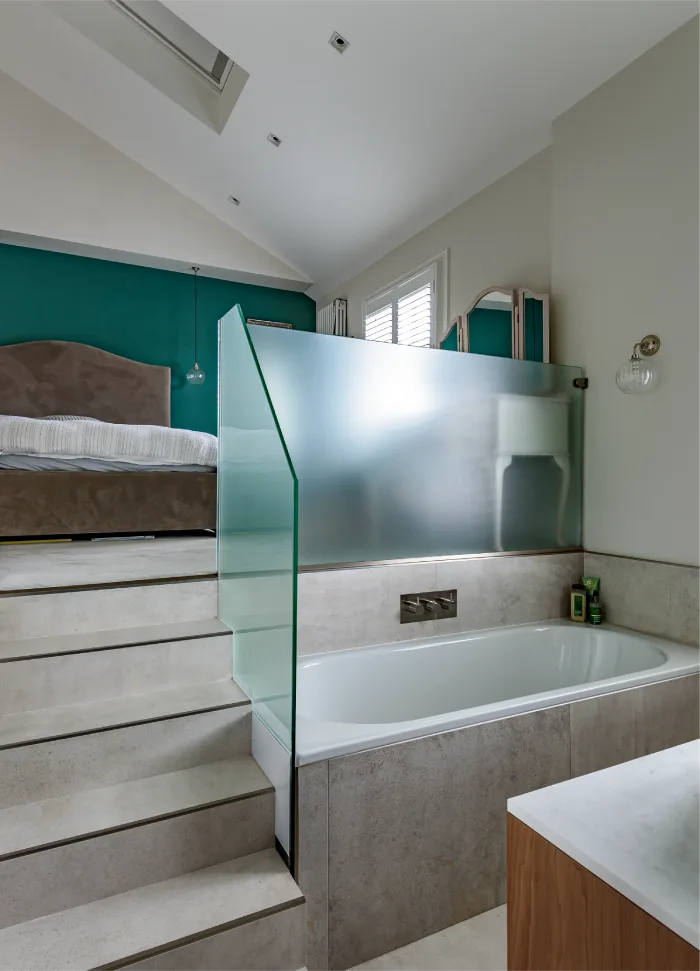 Modern loft-style bathroom with steps leading to a bedroom, featuring a sleek tub and frosted glass partition.