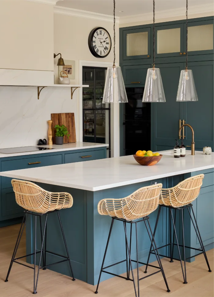 Stylish kitchen with teal cabinets, pendant lights, and a white island featuring wicker bar stools.