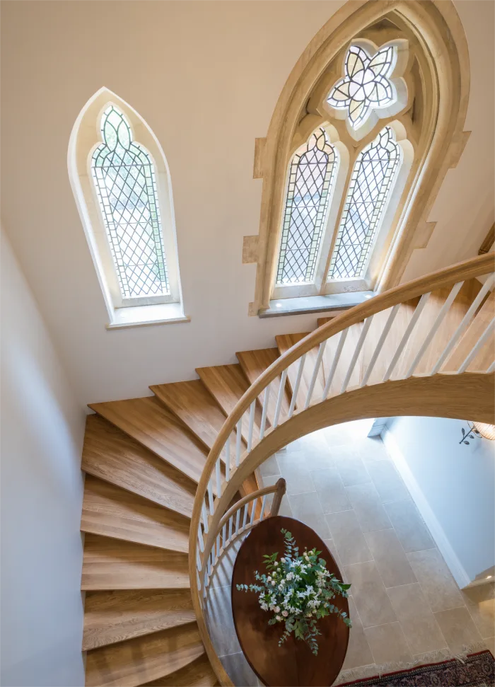 Elegant spiral staircase with wooden steps and decorative arched windows bringing natural light to the interior.