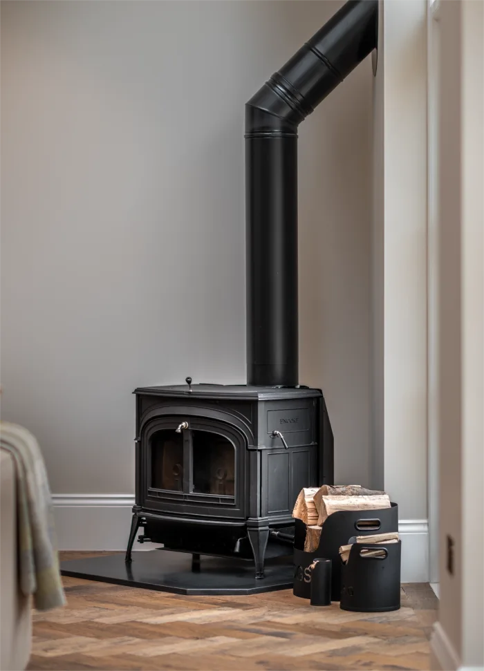 Cozy black wood-burning stove with a chimney pipe, firewood, and a rustic storage basket on a wooden floor.