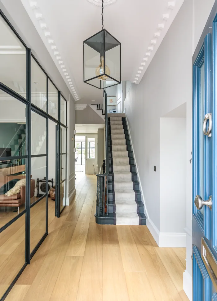 Elegant hallway with a modern lantern chandelier, glass-paneled doors, and a staircase leading to the upper floor.