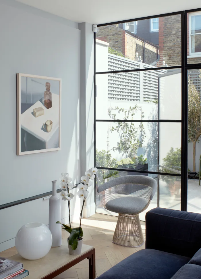 Bright living area with modern decor, large glass panels, and a cozy chair overlooking a private garden.