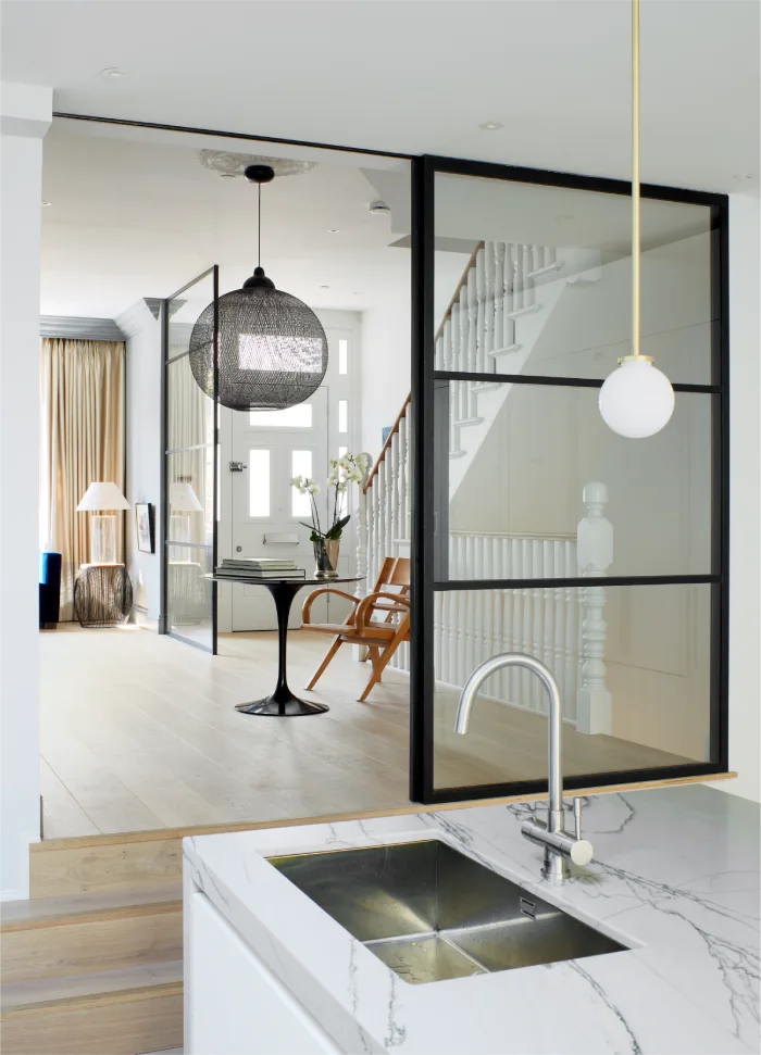 Modern kitchen sink with marble countertop and a view of a stylish hallway with glass partitions.