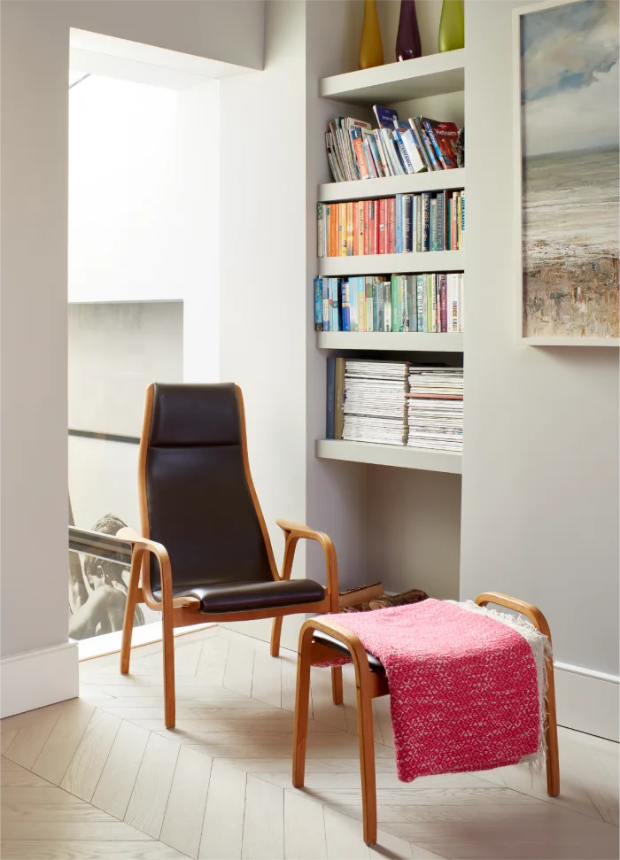 Cozy reading nook with a modern leather chair, vibrant pink throw, and built-in bookshelf filled with colorful books.