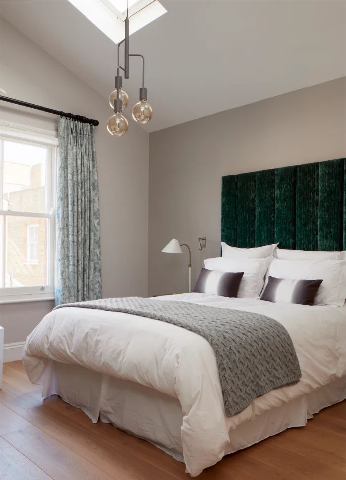 Cozy bedroom with a modern chandelier, green upholstered headboard, white bedding, and a textured gray throw blanket.