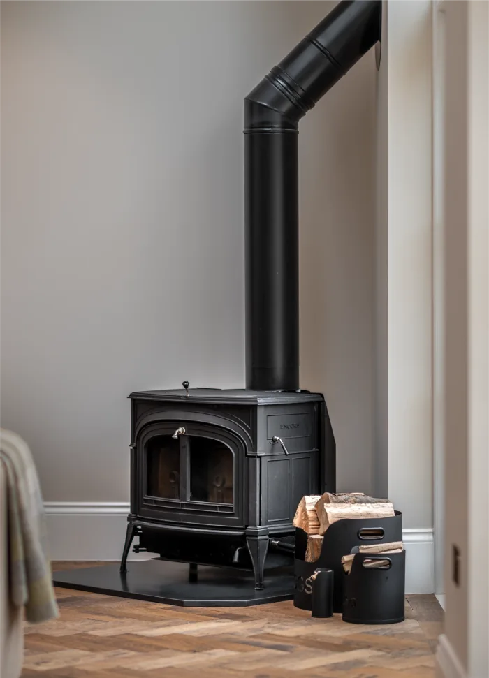 Charming black wood-burning stove with logs and accessories, set against a neutral wall and herringbone wooden floor.