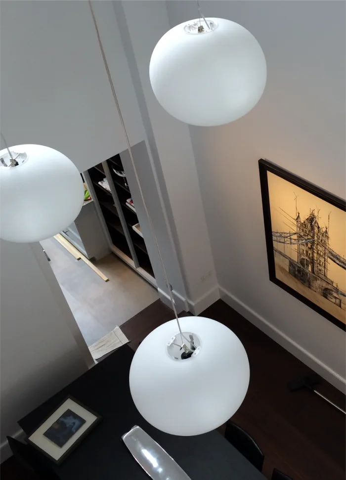 View of modern white pendant lights suspended over a dining area with an artistic Tower Bridge wall frame.