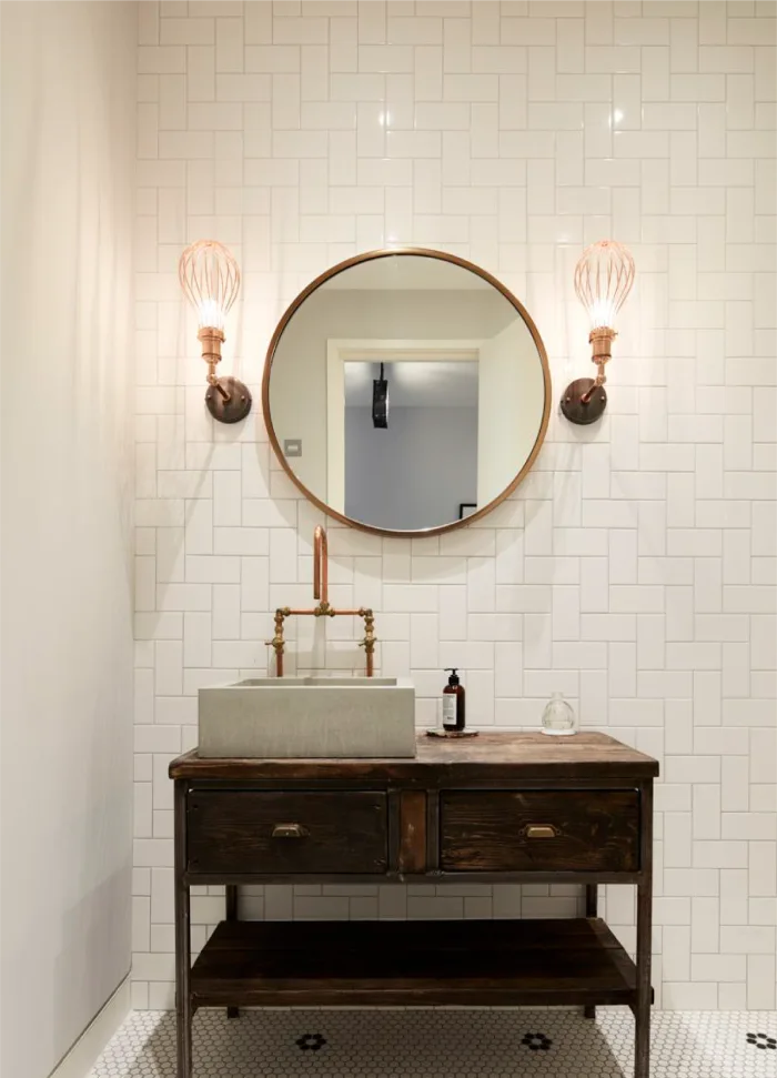 Elegant bathroom with a vintage-style wooden vanity, round mirror, industrial sconces, and white subway tile walls.