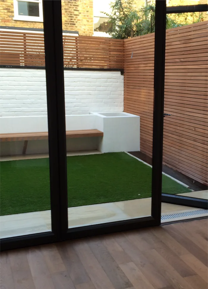 Cozy outdoor patio with a mix of artificial grass, wooden fencing, and a built-in bench for relaxing moments.