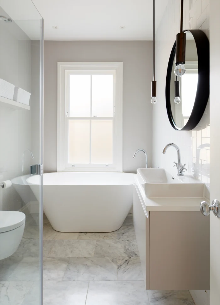 Modern bathroom with a freestanding white bathtub, marble flooring, a floating vanity, and a round mirror.