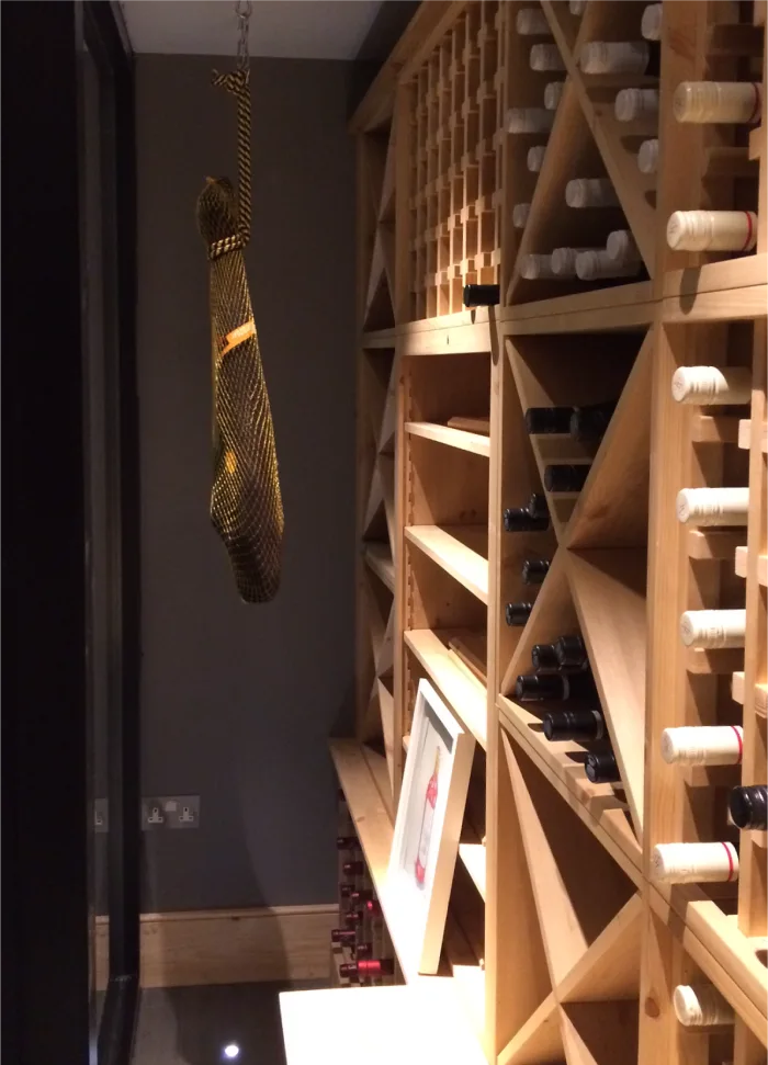 Wine storage area featuring wooden shelves with an assortment of wine bottles and a decorative hanging cured ham in netting.