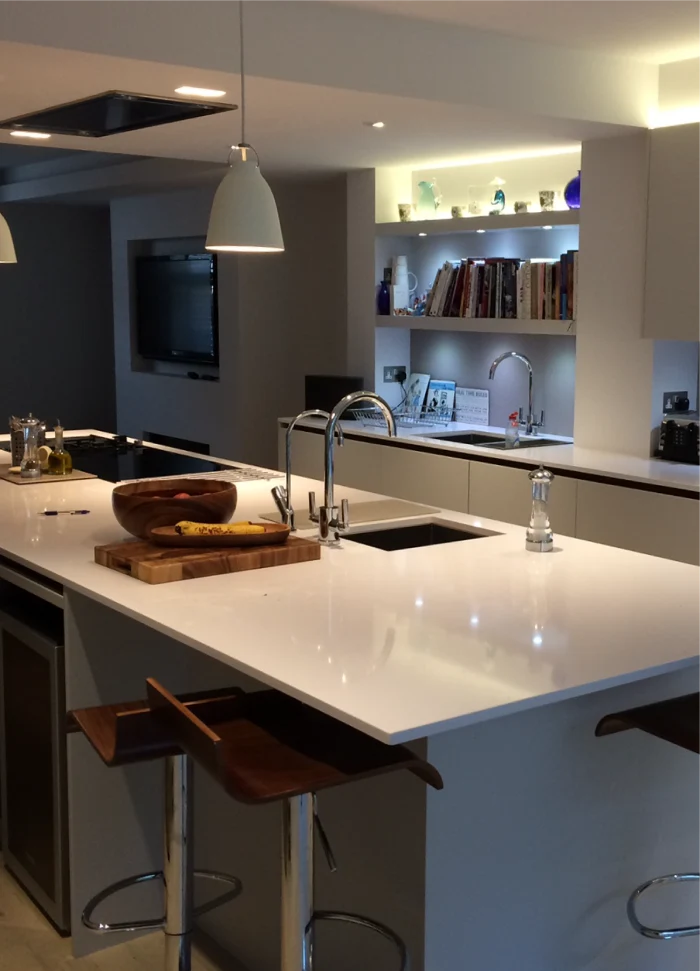 Modern kitchen with sleek counters, hanging lights, built-in shelves, and wooden stools under the island.