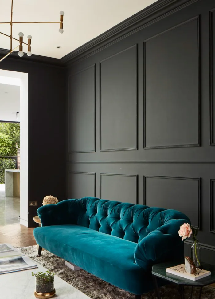 Elegant living area featuring a teal tufted sofa, dark paneled walls, and a modern gold light fixture.