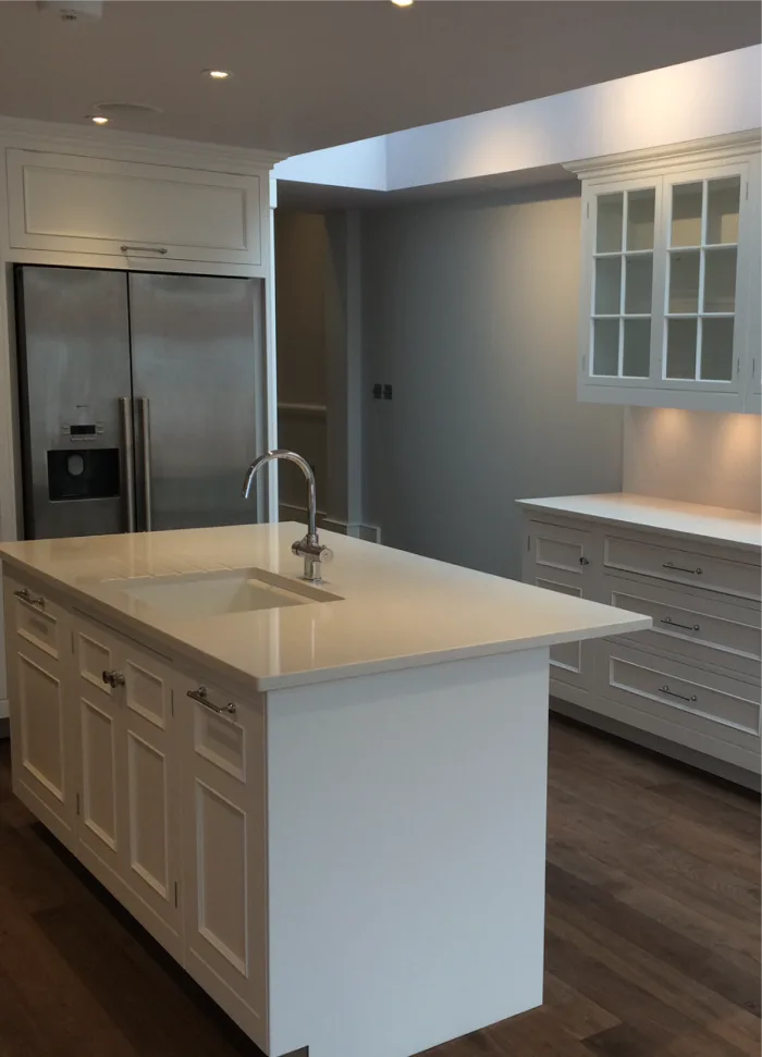 A sleek modern kitchen with a bright white island featuring a built-in sink, complemented by clean cabinetry and stainless steel appliances, illuminated under soft recessed lighting.