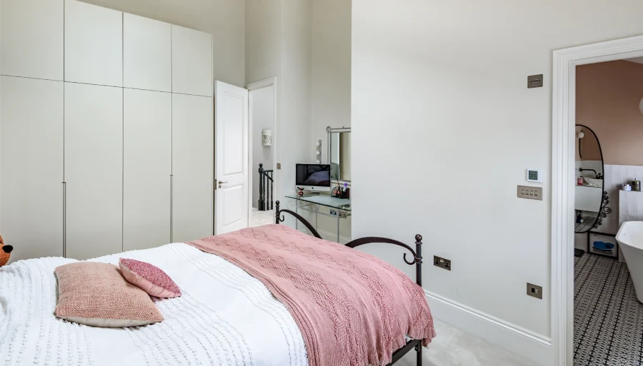 Cozy bedroom with blush accents, sleek wardrobes, a vanity corner, and a serene neutral-toned design.