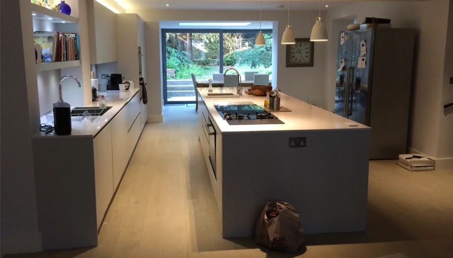 Spacious modern kitchen with large island, built-in shelving, pendant lights, and sliding doors to garden view.