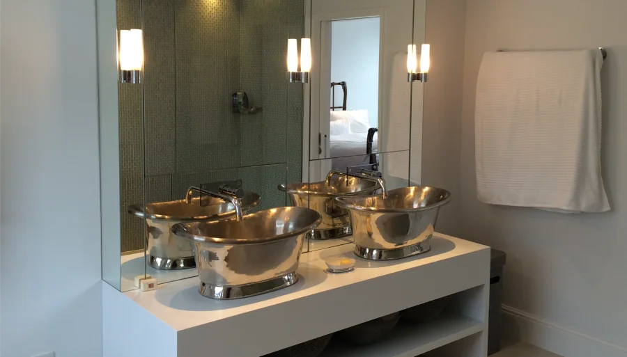 Luxurious double vanity featuring metallic vessel sinks, illuminated by modern wall sconces, and complemented by a sleek mirror backsplash.