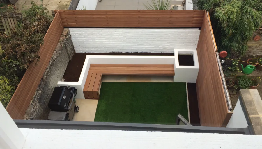 A compact and modern backyard with wooden fencing, a built-in bench, and a small patch of artificial grass, creating a clean and low-maintenance outdoor seating area.